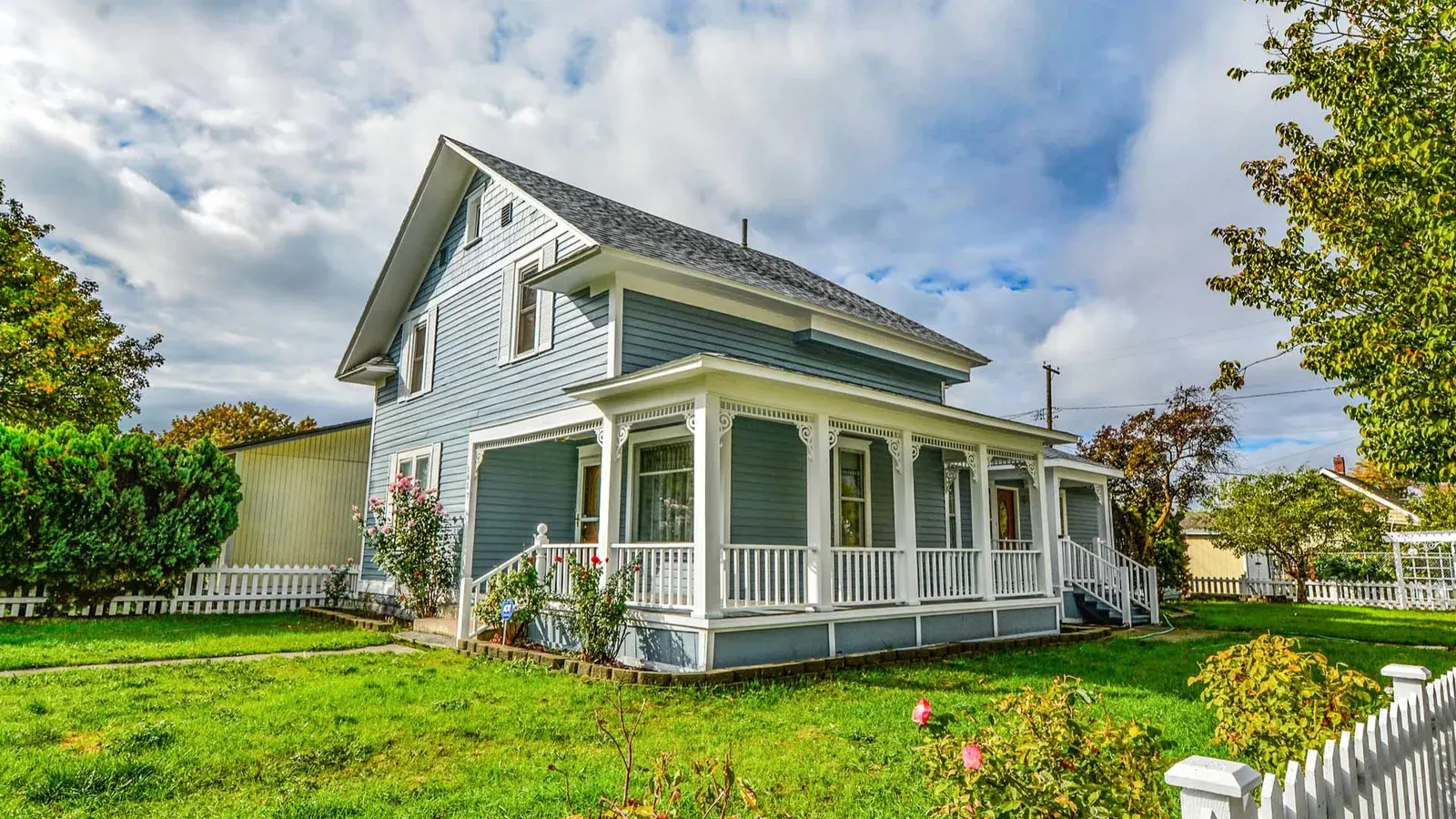 Blue farmhouse with a wraparound porch and a white picket fence