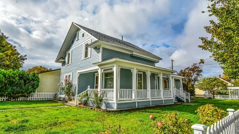 Blue farmhouse with a wraparound porch and a white picket fence