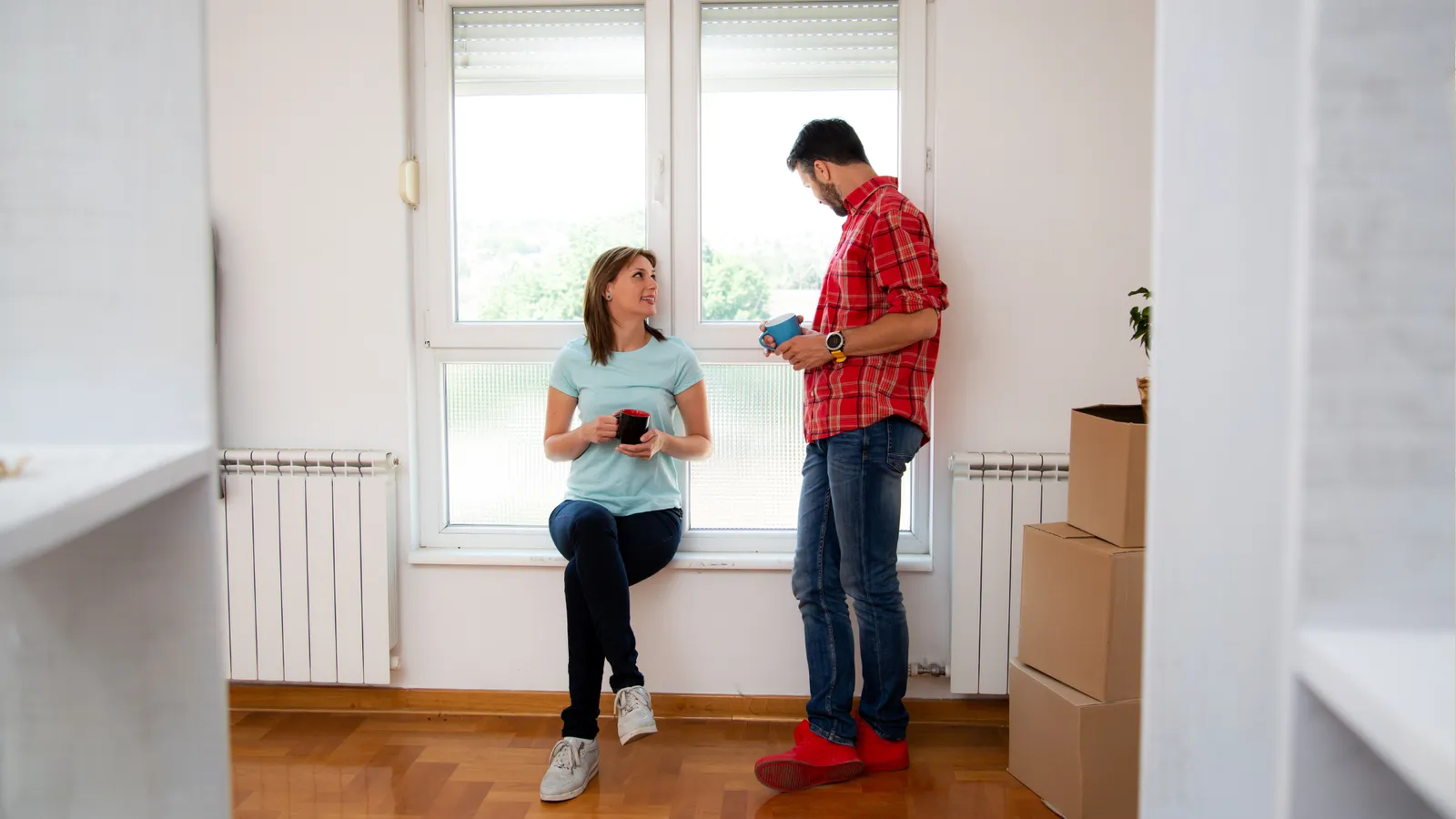 Couple talking by a sunny window in an empty room with moving boxes