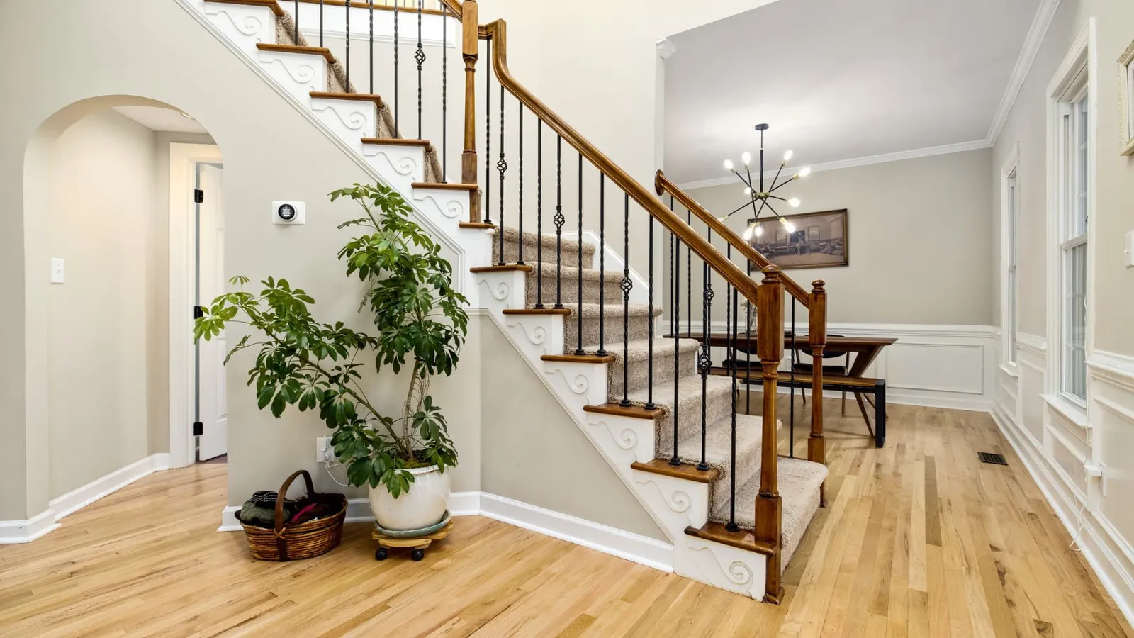 Bright entry hall with a wood staircase, a potted plant, and a dining room beyond