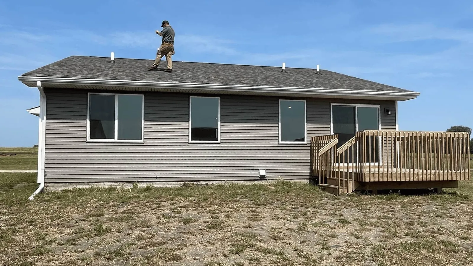Inspector walking the roof of a gray ranch home with a back deck