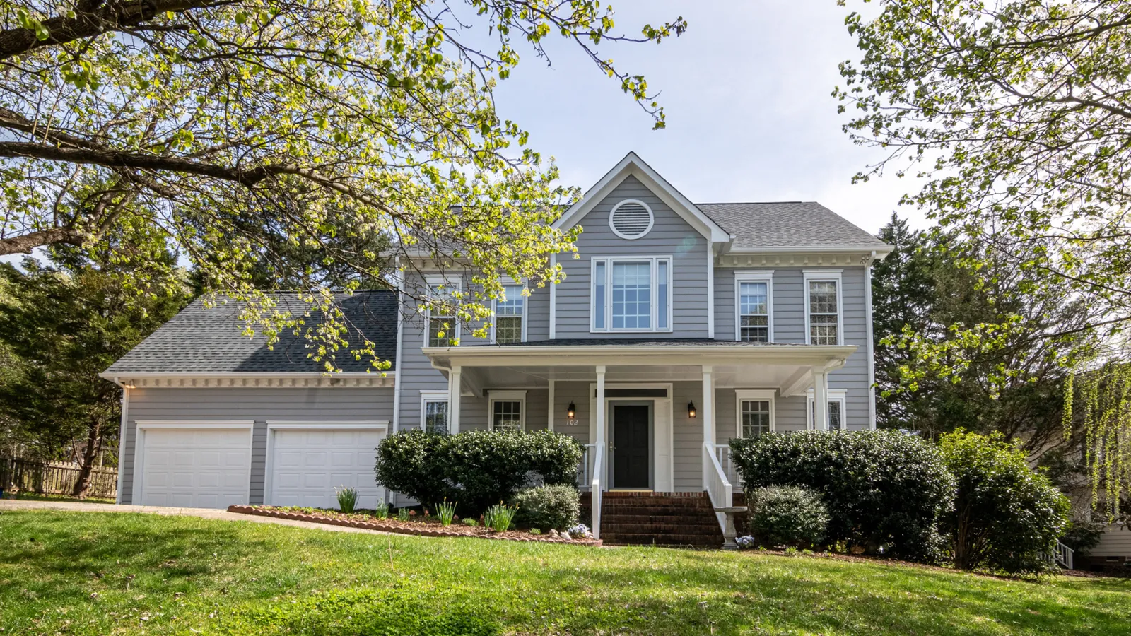 Blue two-story home with a covered porch and a large green lawn