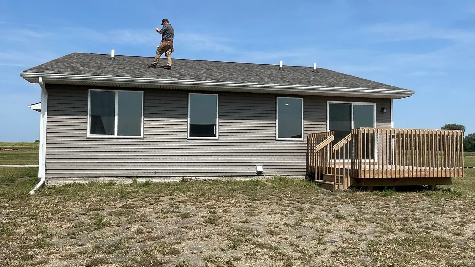 Inspector standing on the roof of a gray ranch home with a back deck