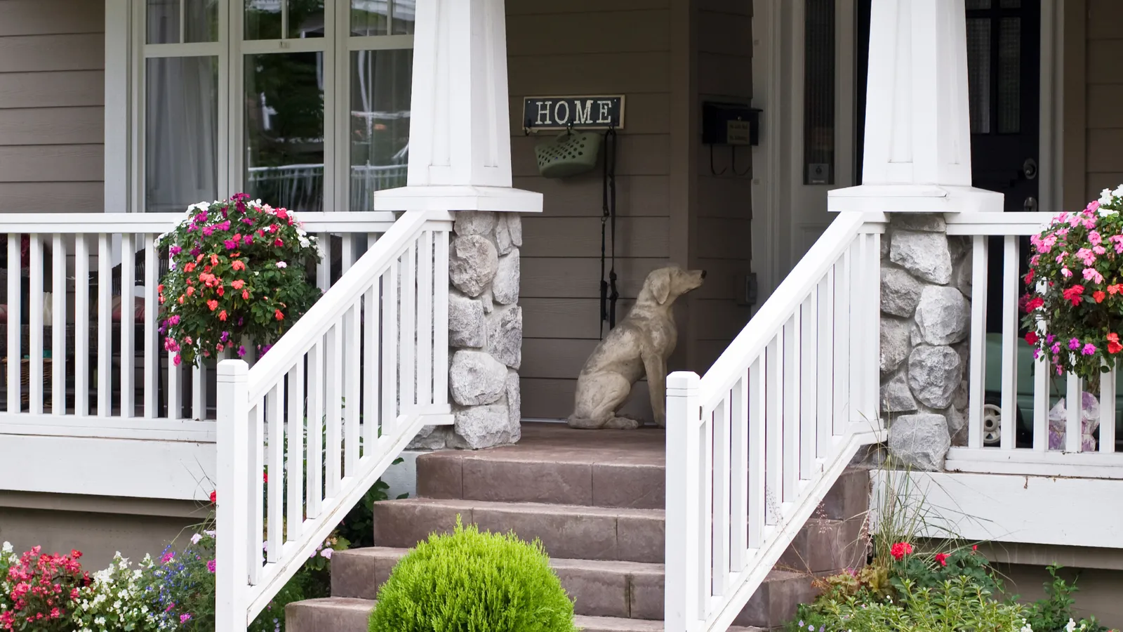 Front porch steps with white railings, flower baskets, and a dog on the landing