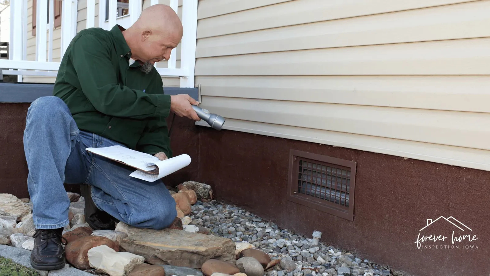 Inspector with a clipboard kneeling beside a crawl space vent