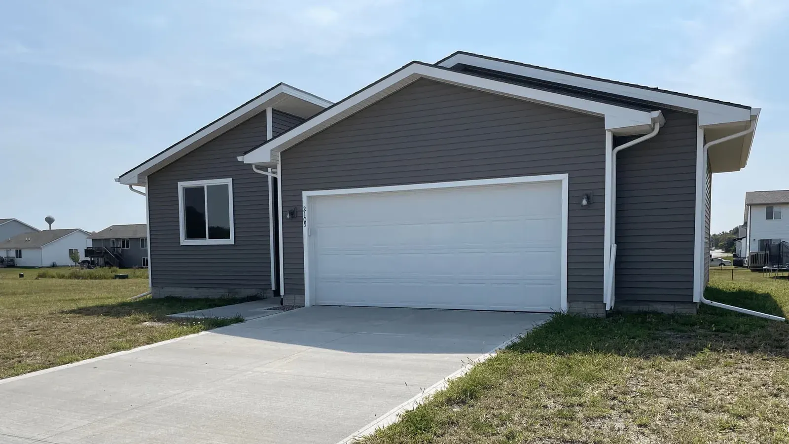Newly built gray home with a white garage door and a fresh driveway