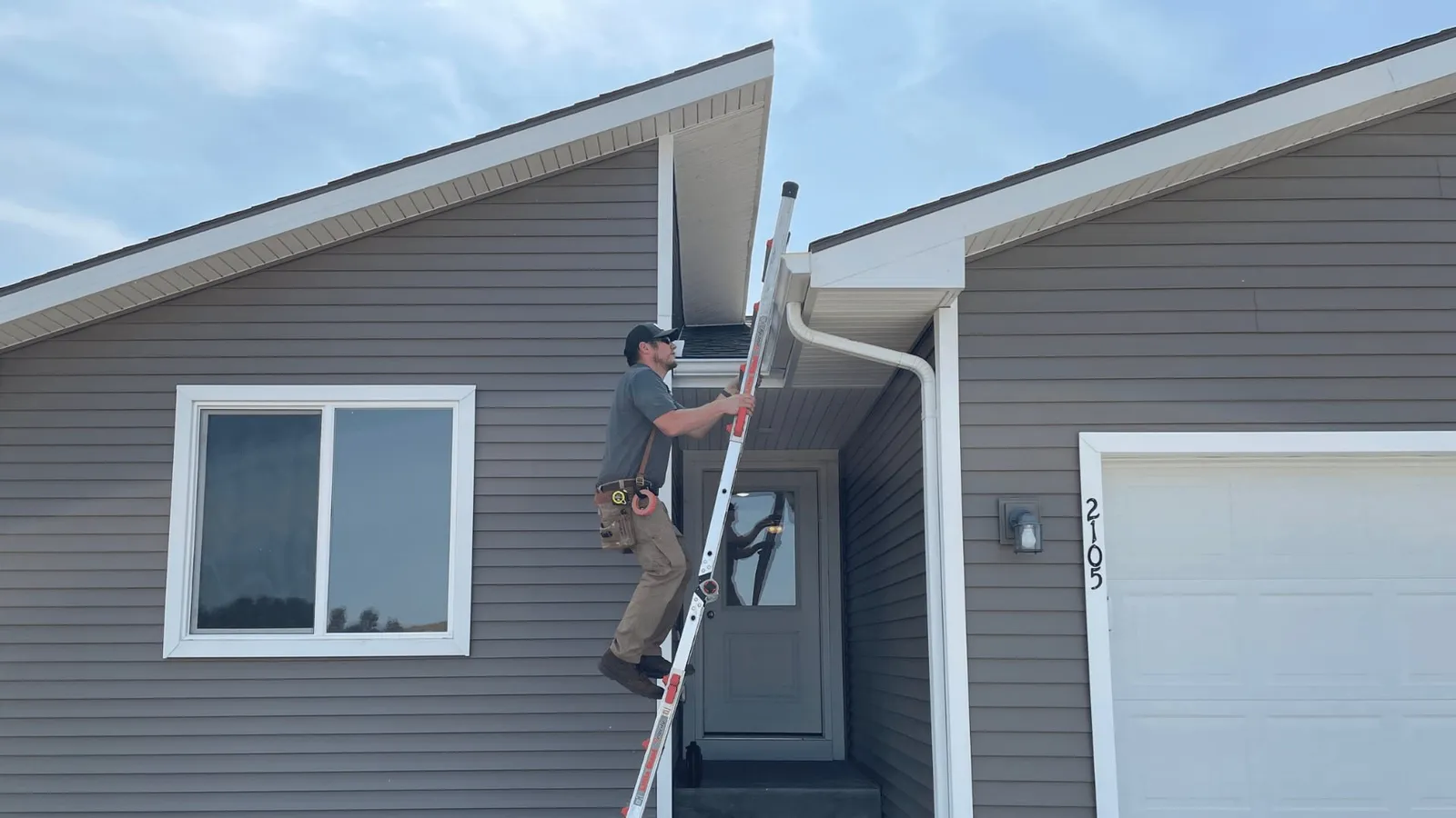 Inspector on a ladder checking the gutter of a gray home