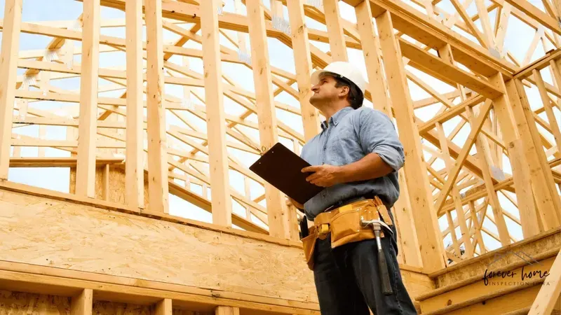 Inspector in a hard hat reviewing a clipboard inside new wood framing