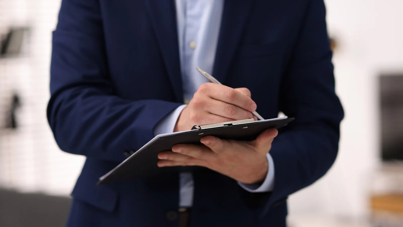 Person in a suit writing notes on a clipboard