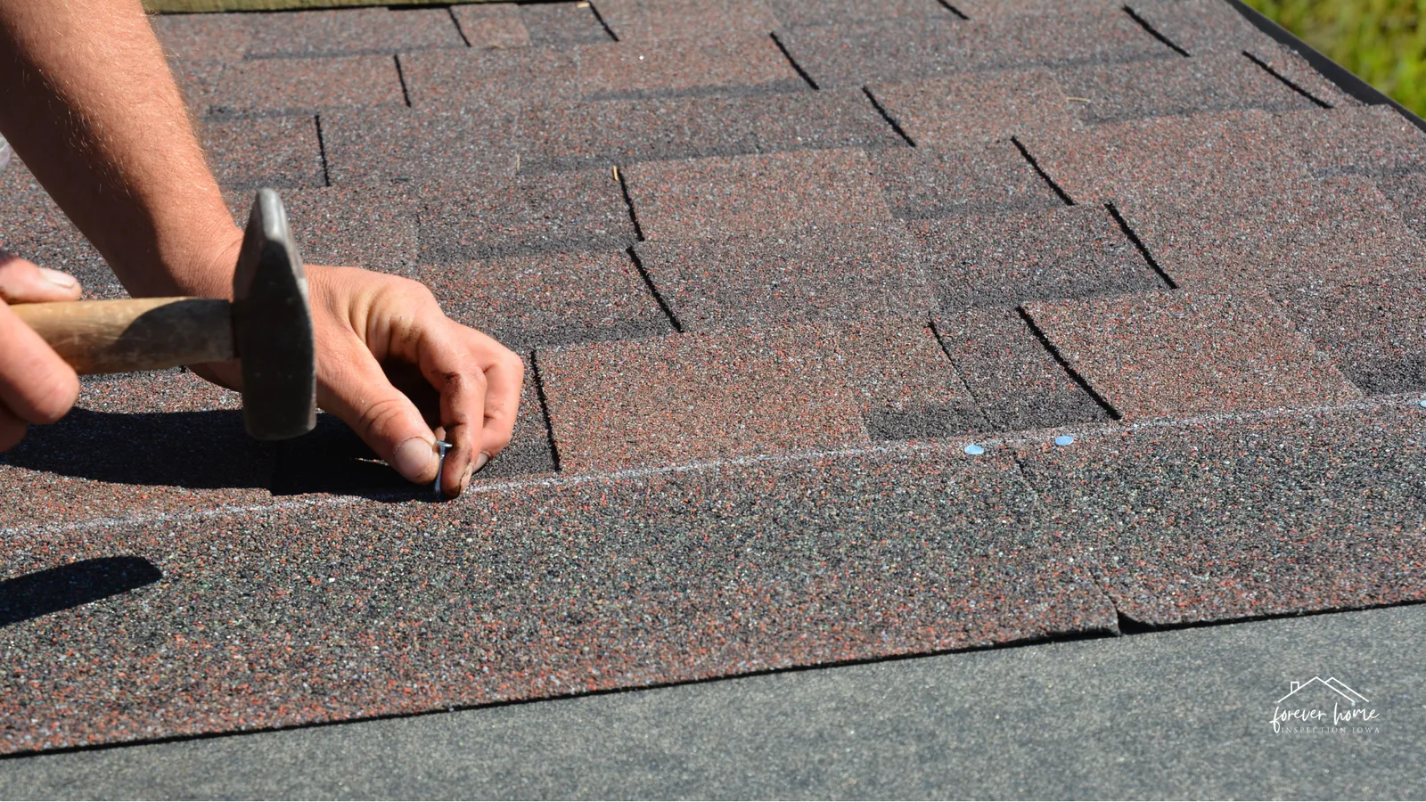 Hands nailing down a roof shingle with a hammer