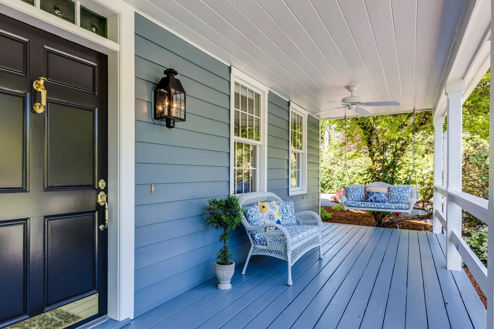Covered front porch with a navy door, a bench, and porch swing