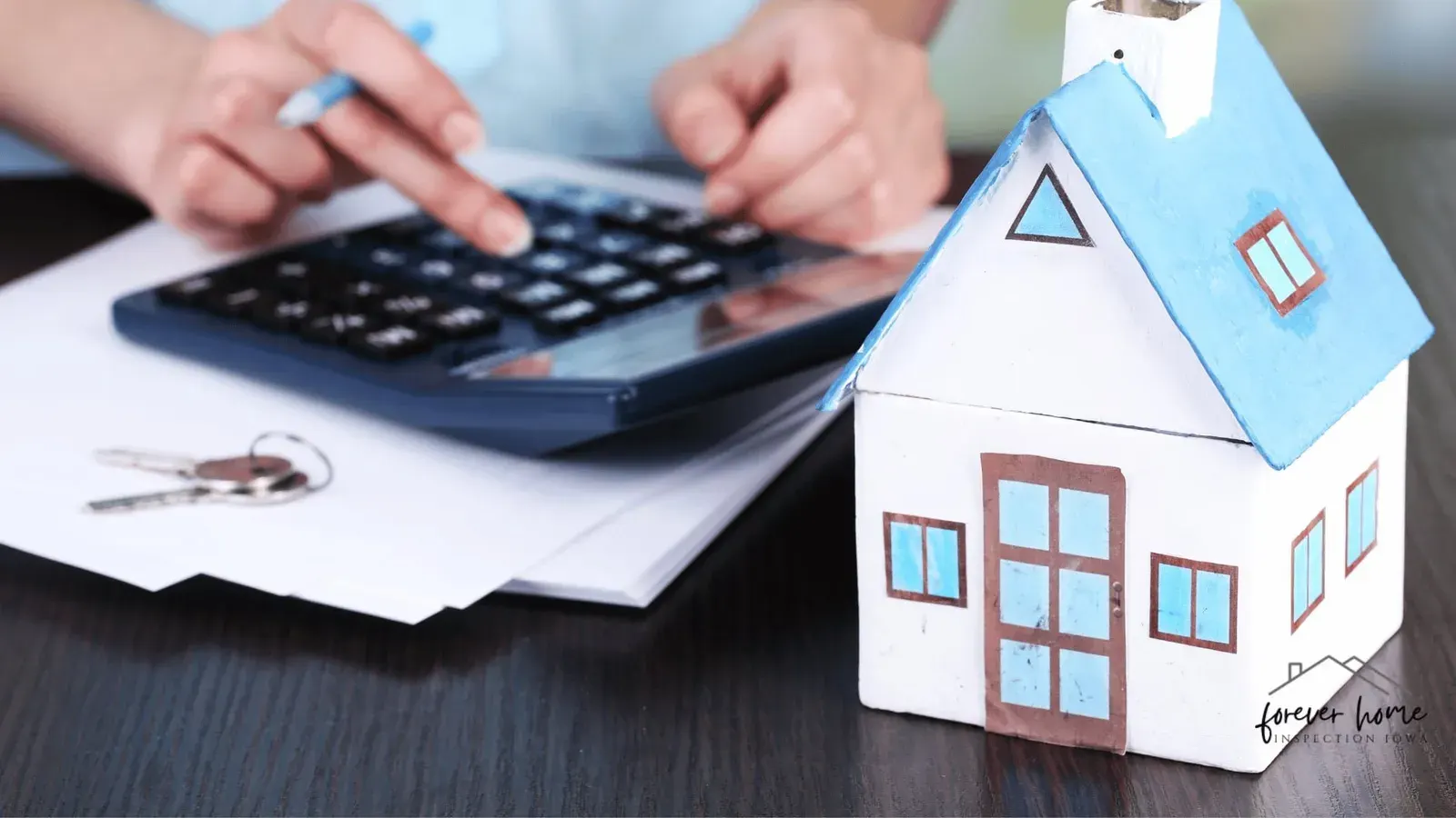 Hands using a calculator next to a small paper house and keys