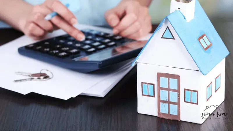 Hands using a calculator next to a small paper house and keys