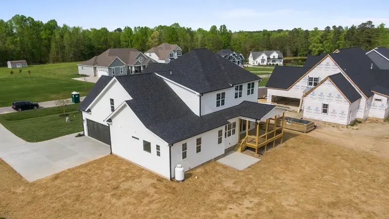Aerial view of a newly built white home with a dark roof in a new subdivision