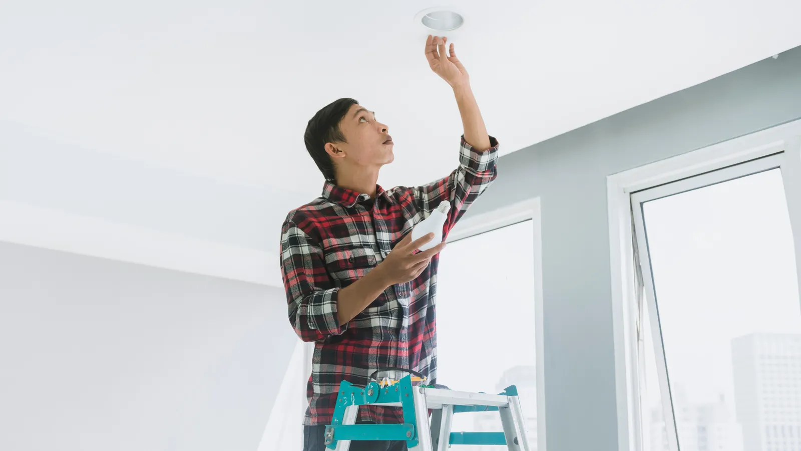 Man on a step stool testing a ceiling smoke detector