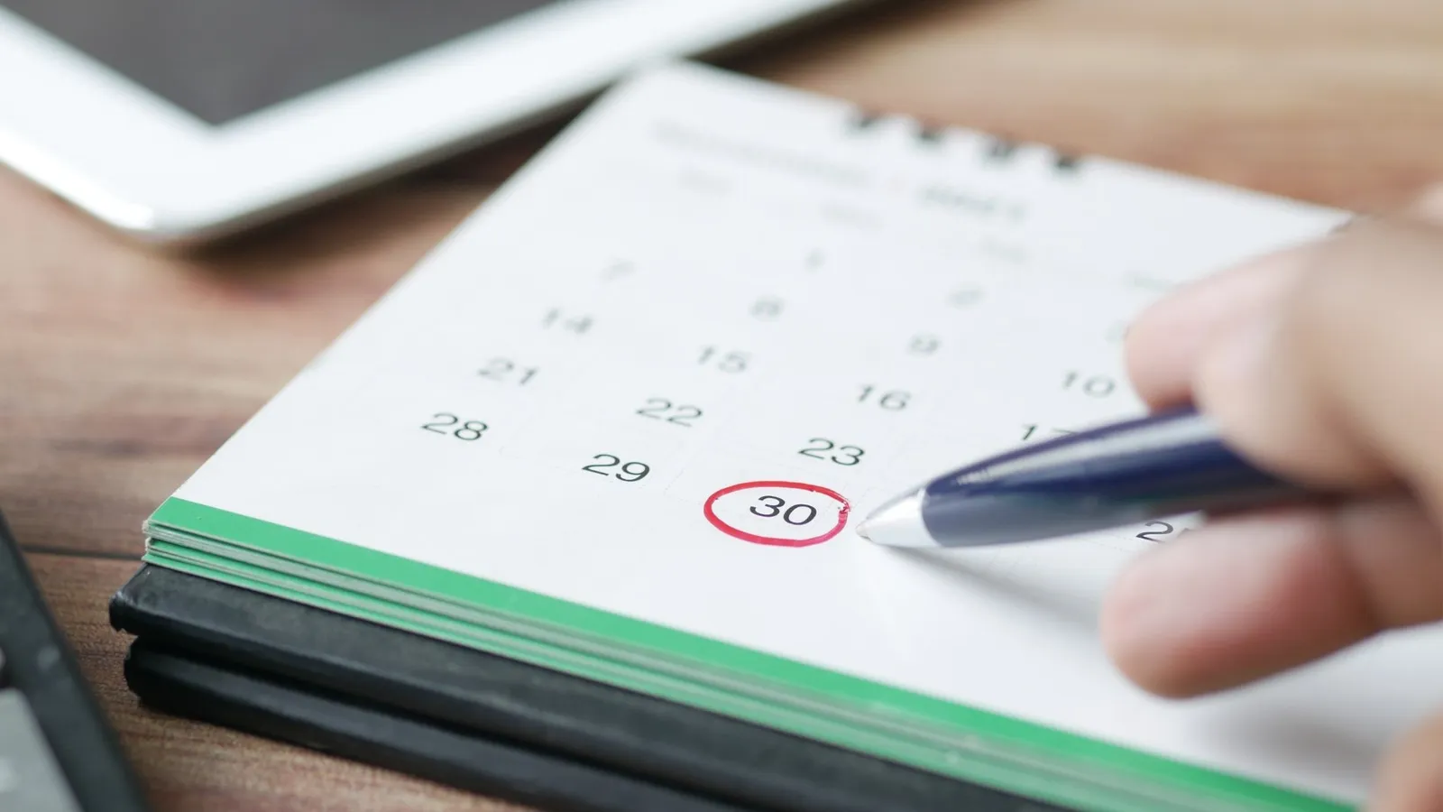 Hand circling a date on a desk calendar