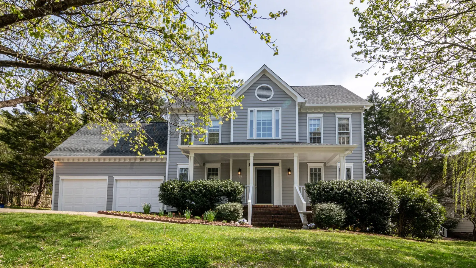 Blue two-story home with a covered porch and a large green lawn
