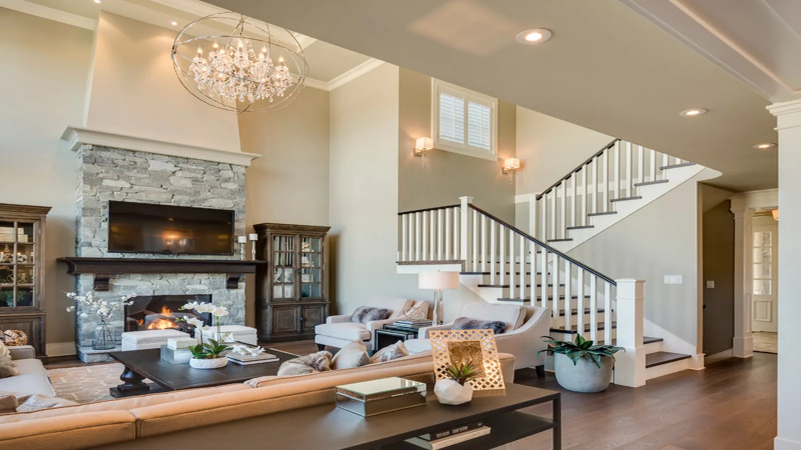 Open living room with a stone fireplace, chandelier, and staircase