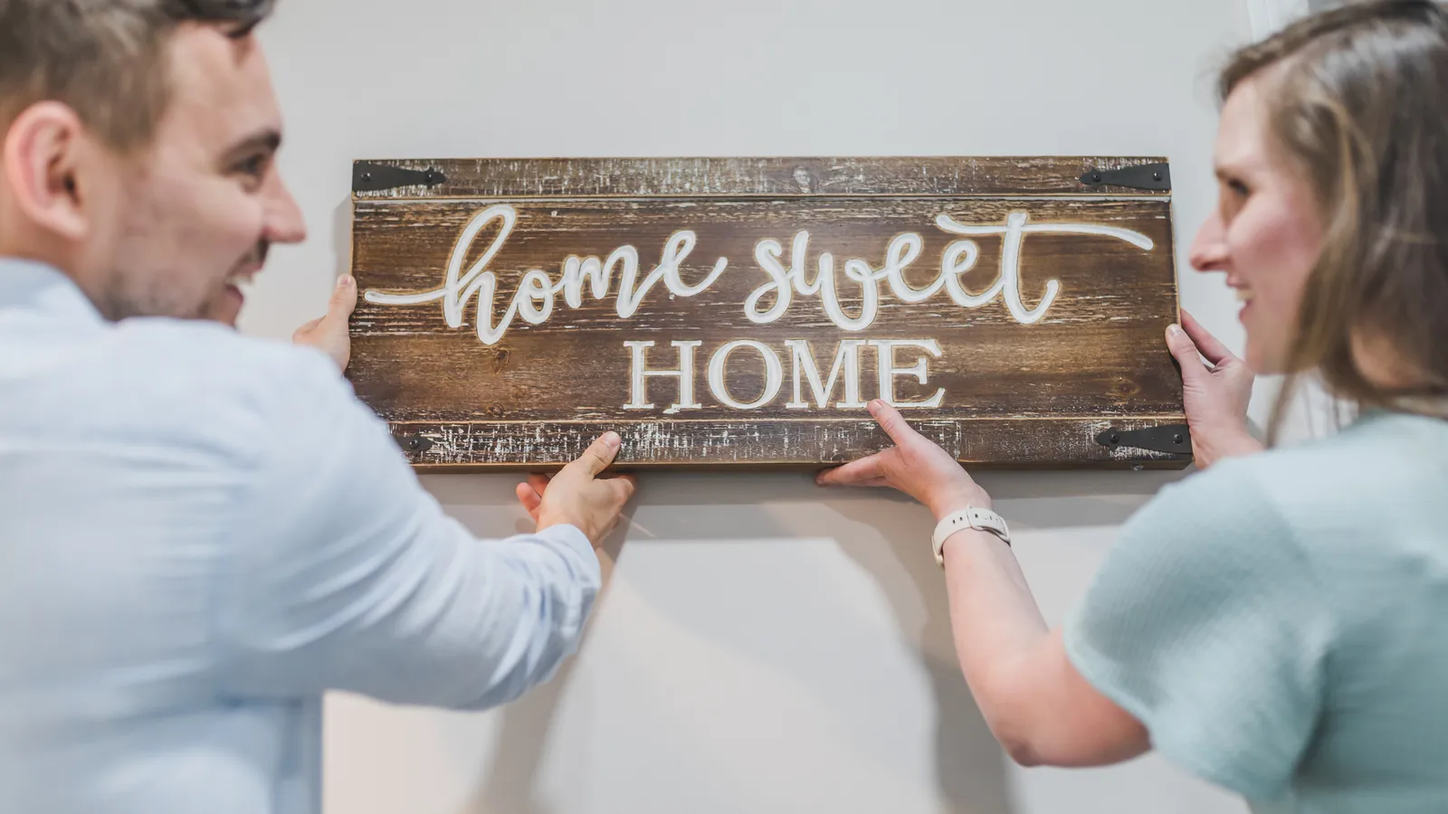 Couple hanging a Home Sweet Home sign on a wall