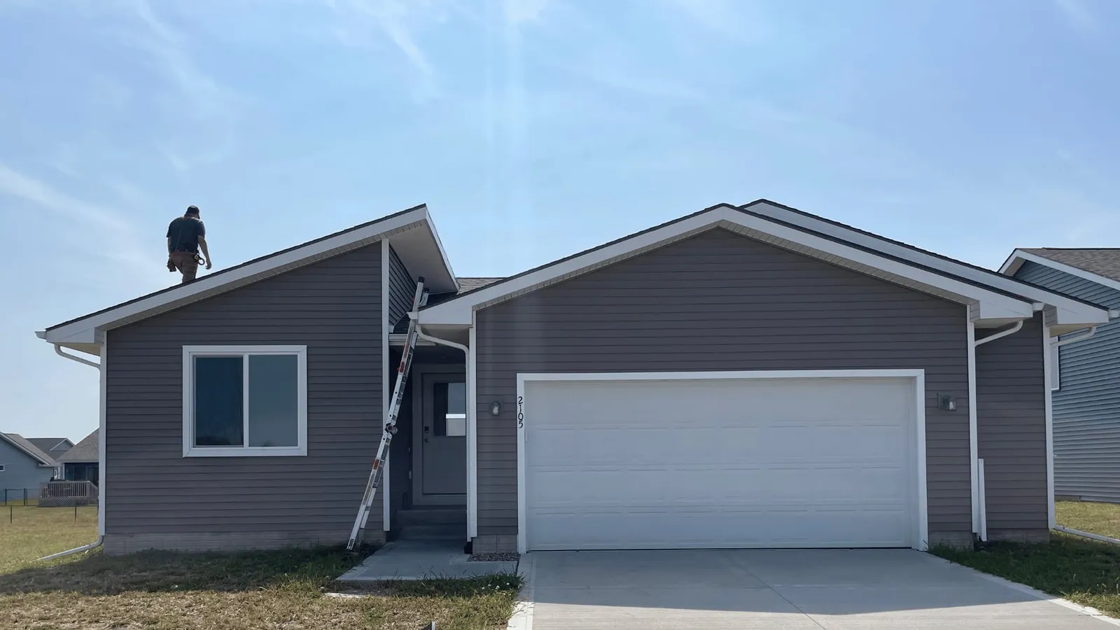 Inspector on the roof of a gray home with a white garage door