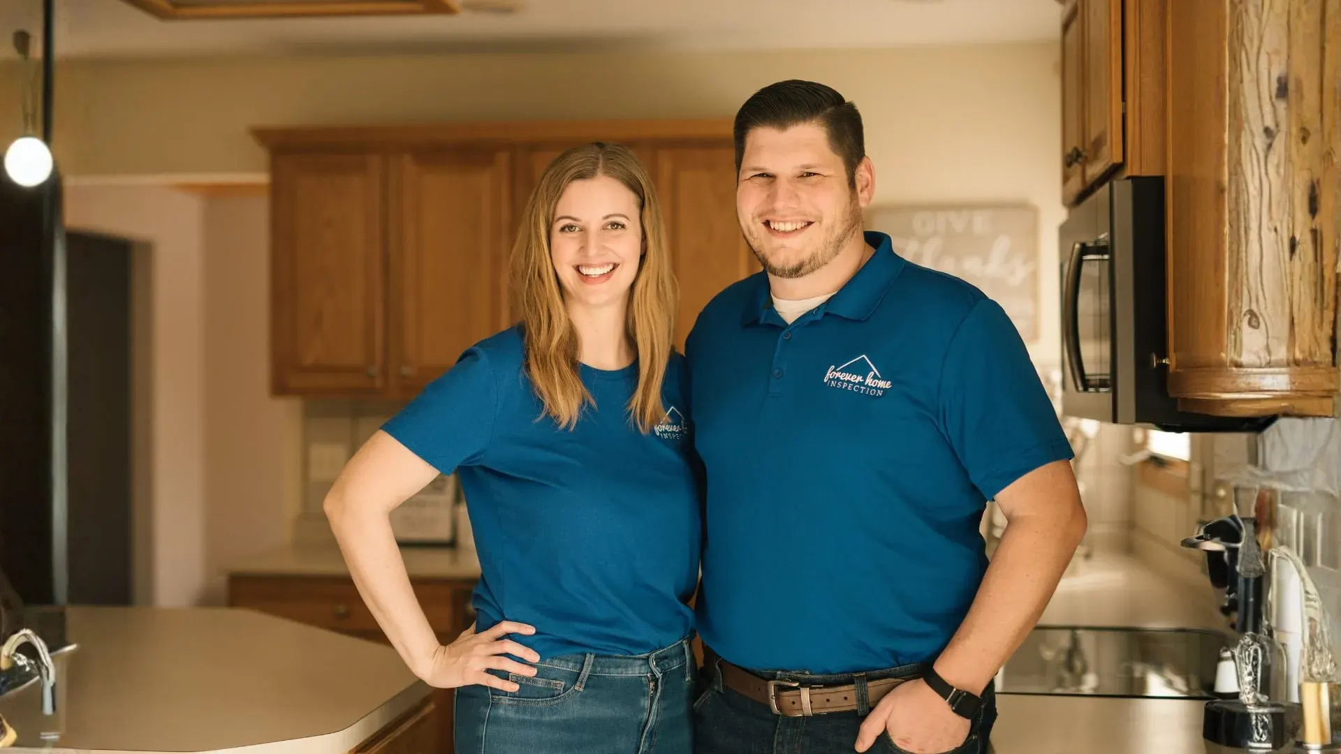 Matt and Kalyn Gibson, owners of Forever Home Inspection Iowa, smiling in a kitchen in matching blue company polos