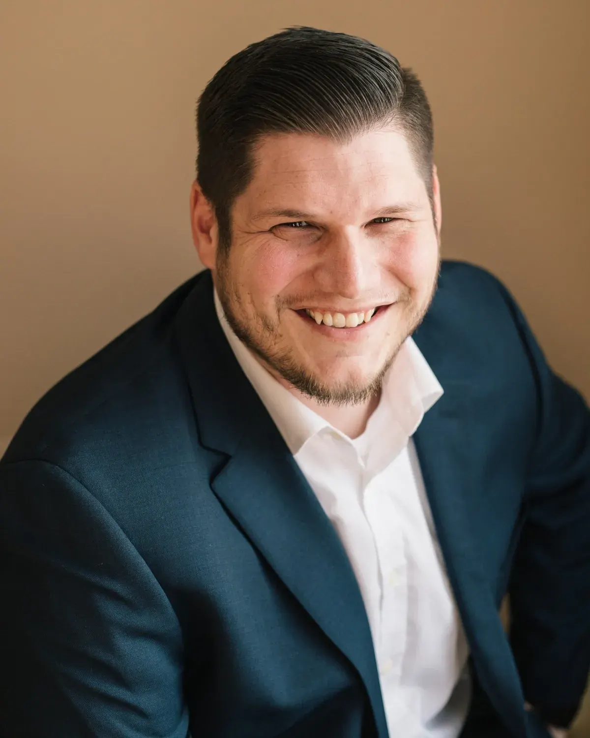 Matt Gibson in a navy blazer against a warm tan background